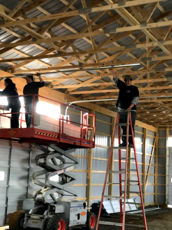 Man in blue jumpsuit fixing garage door mechanism, tools nearby.
