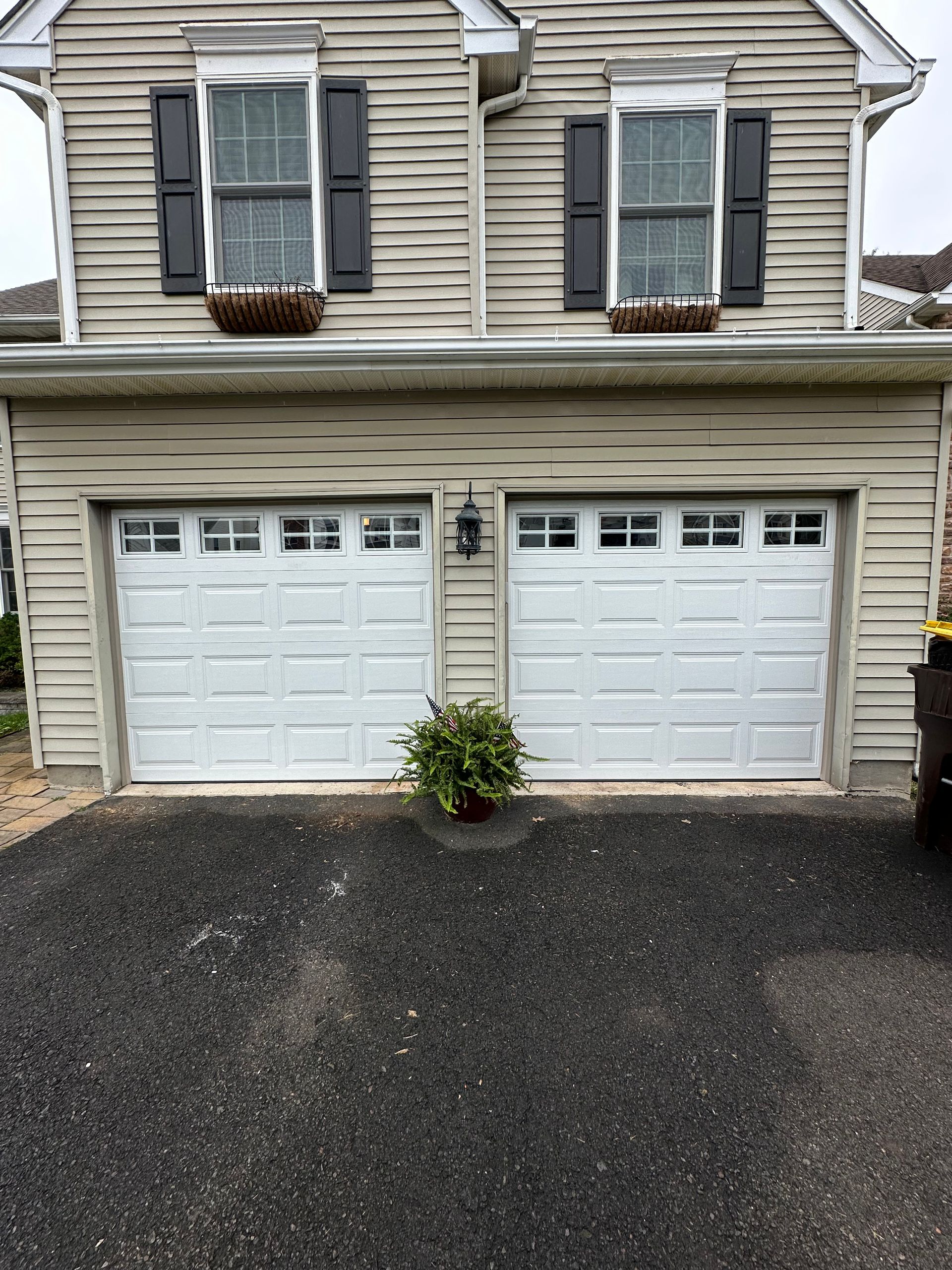 Man on a ladder repairs garage door opener, holding tools. Open garage door, wood ceiling.