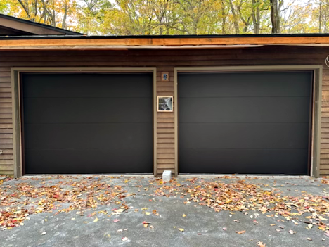 Two workers installing a new gray garage door in front of a house. One is on a ladder.