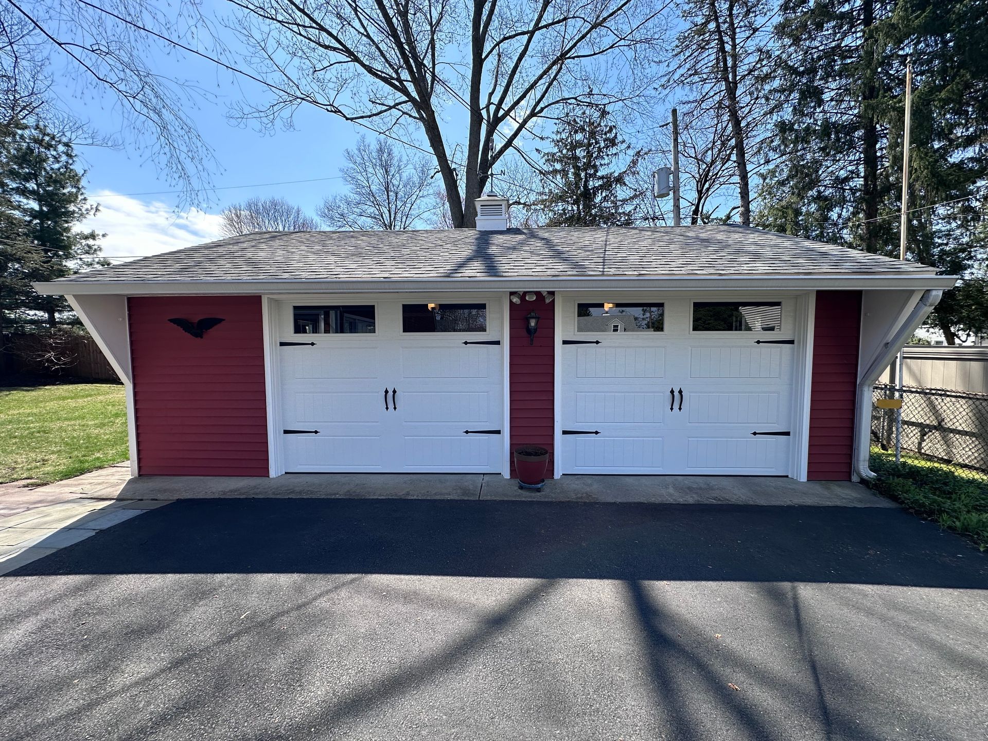Beige garage with white door partially open, driveway, wooden fence, clear sky.