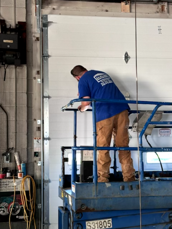A person in a blue uniform repairing a garage door hinge with a wrench.