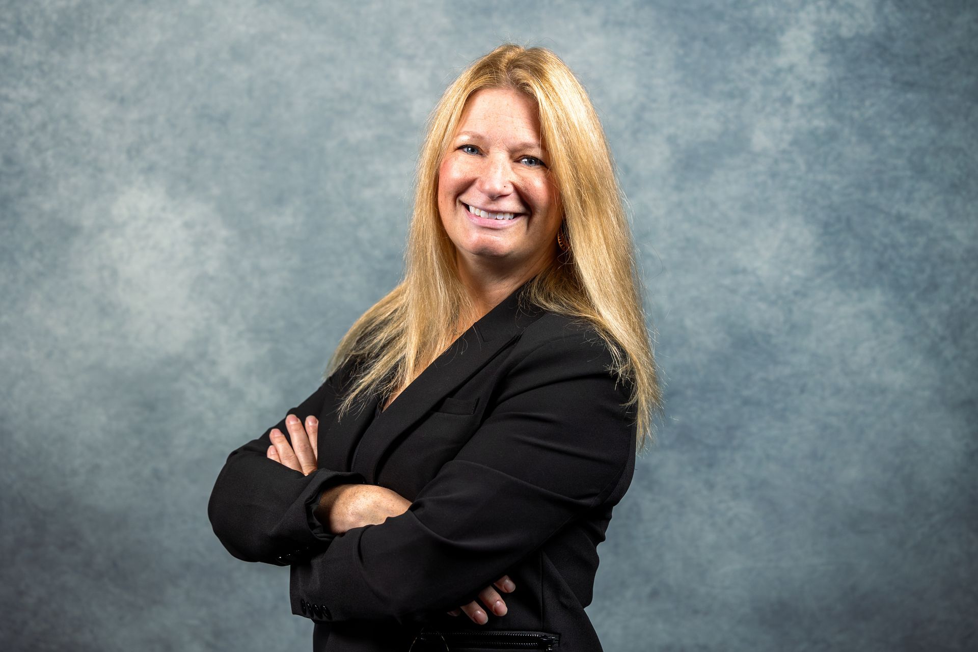 A woman in a black jacket is smiling with her arms crossed