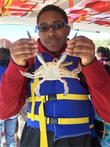 A young boy in a life jacket is holding a crab in his hands.