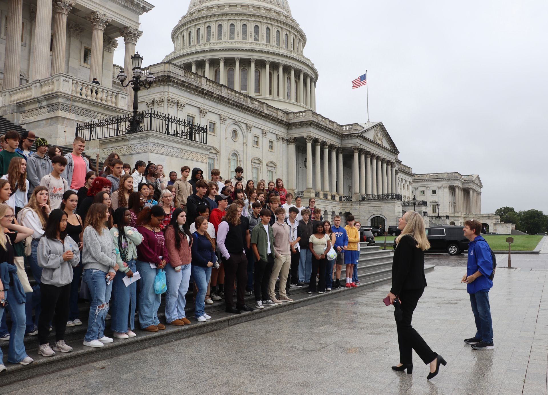 A woman stands in front of a crowd of people in front of the capitol building