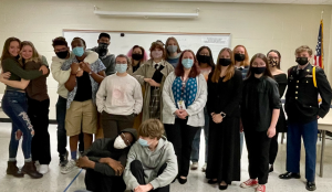 A group of people wearing masks are posing for a picture in a classroom.