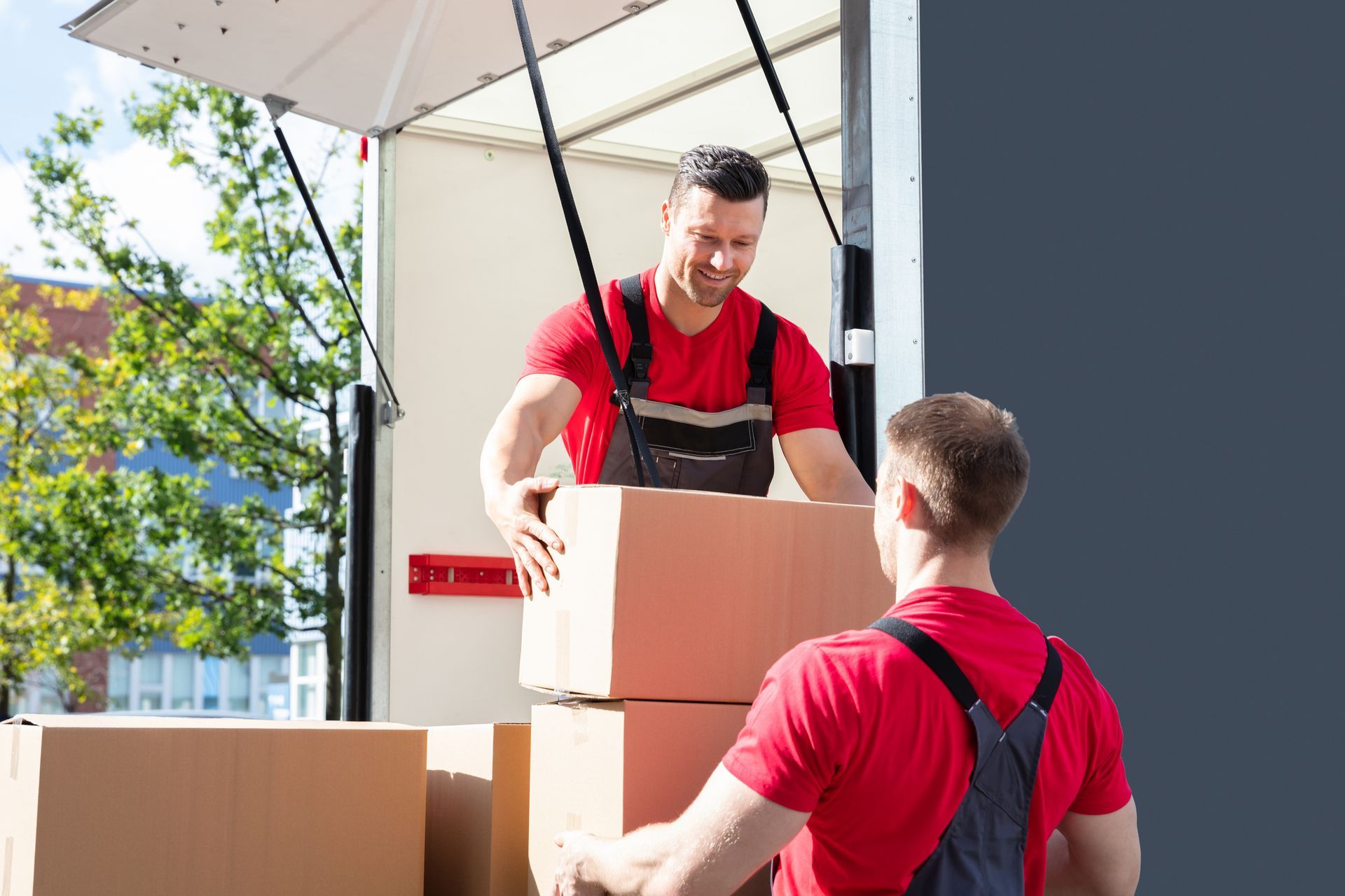 Two men unloading boxes from a moving truck, showcasing full-service movers in action. Two men unloading boxes from a moving truck, showcasing full-service movers in action.
