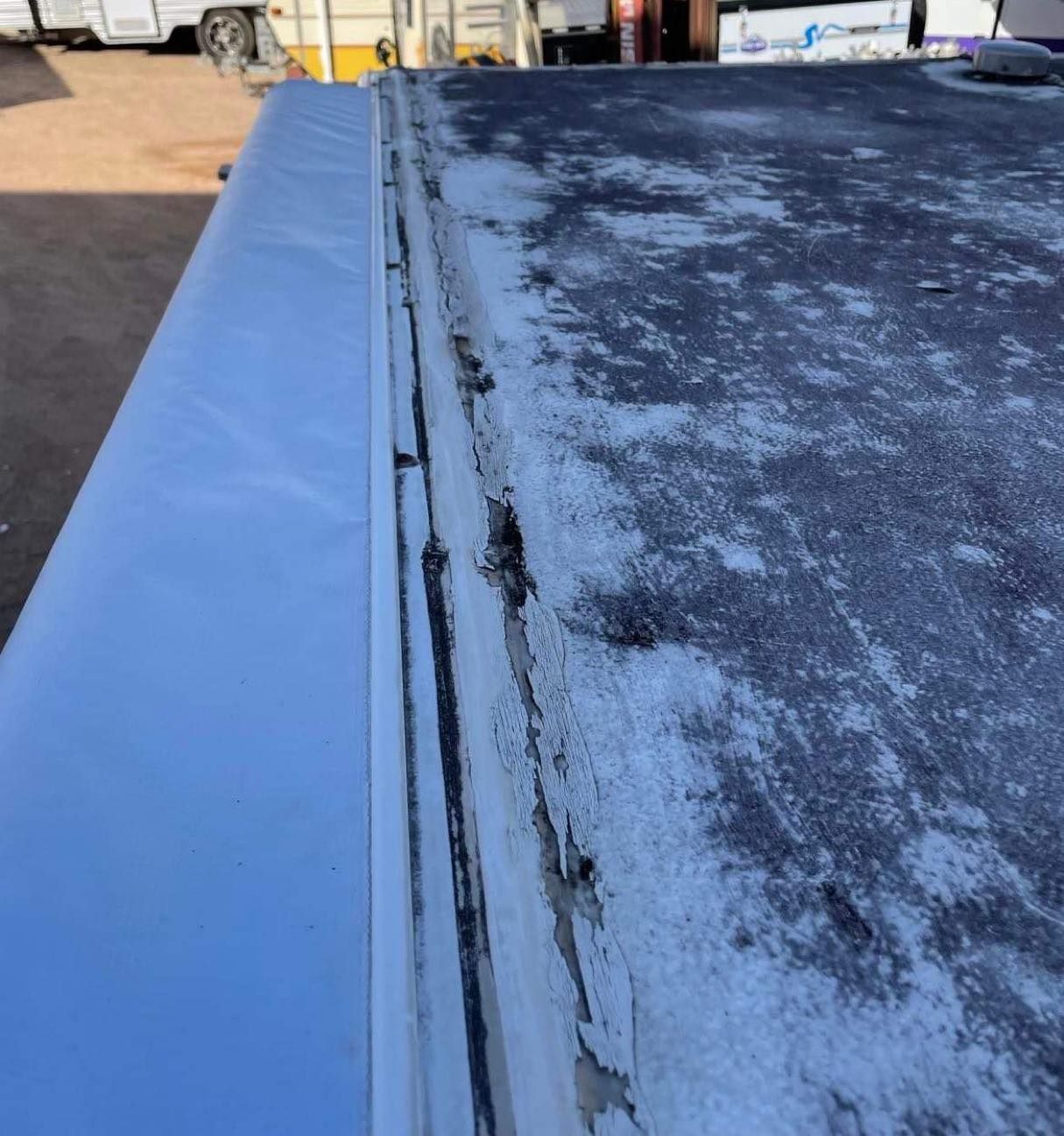 RV roof edge: weathered black roof meets white side panel, with sealant and trim visible.