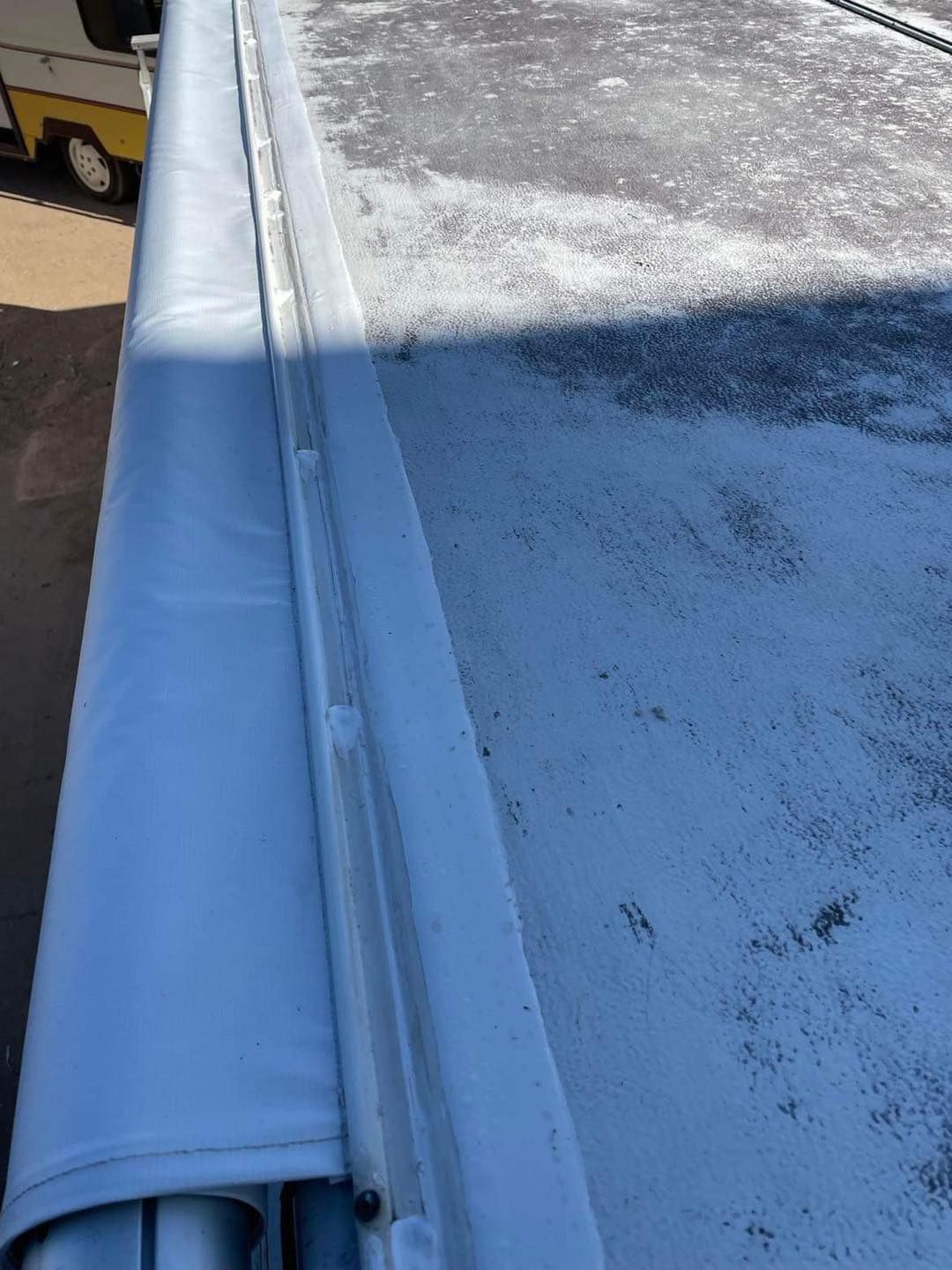 RV roof with a rolled-up awning. Gray awning, weathered white roof.
