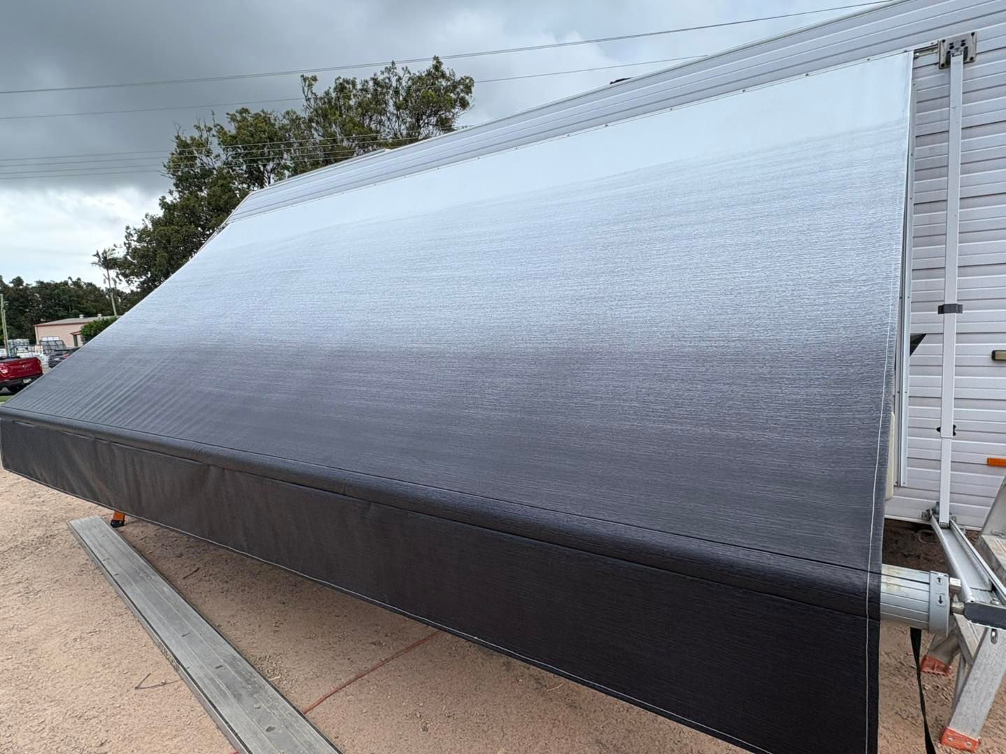 A gray and black retractable awning extended from a house under a cloudy sky.