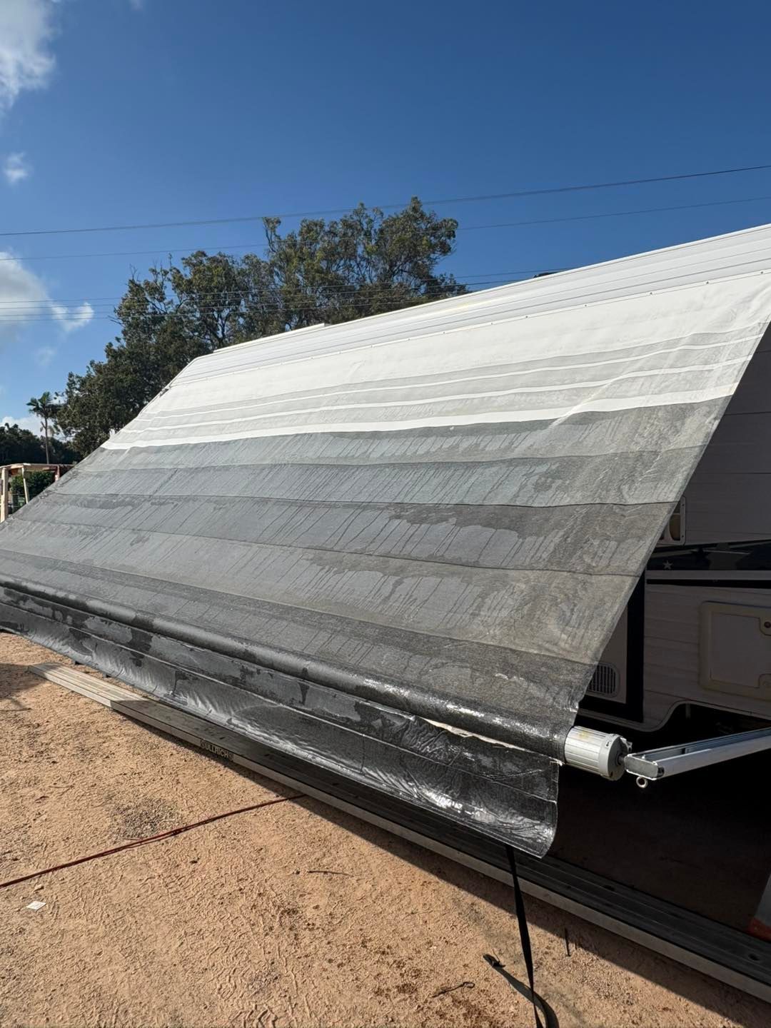 RV awning, faded dark grey to white, extended on a sunny day.