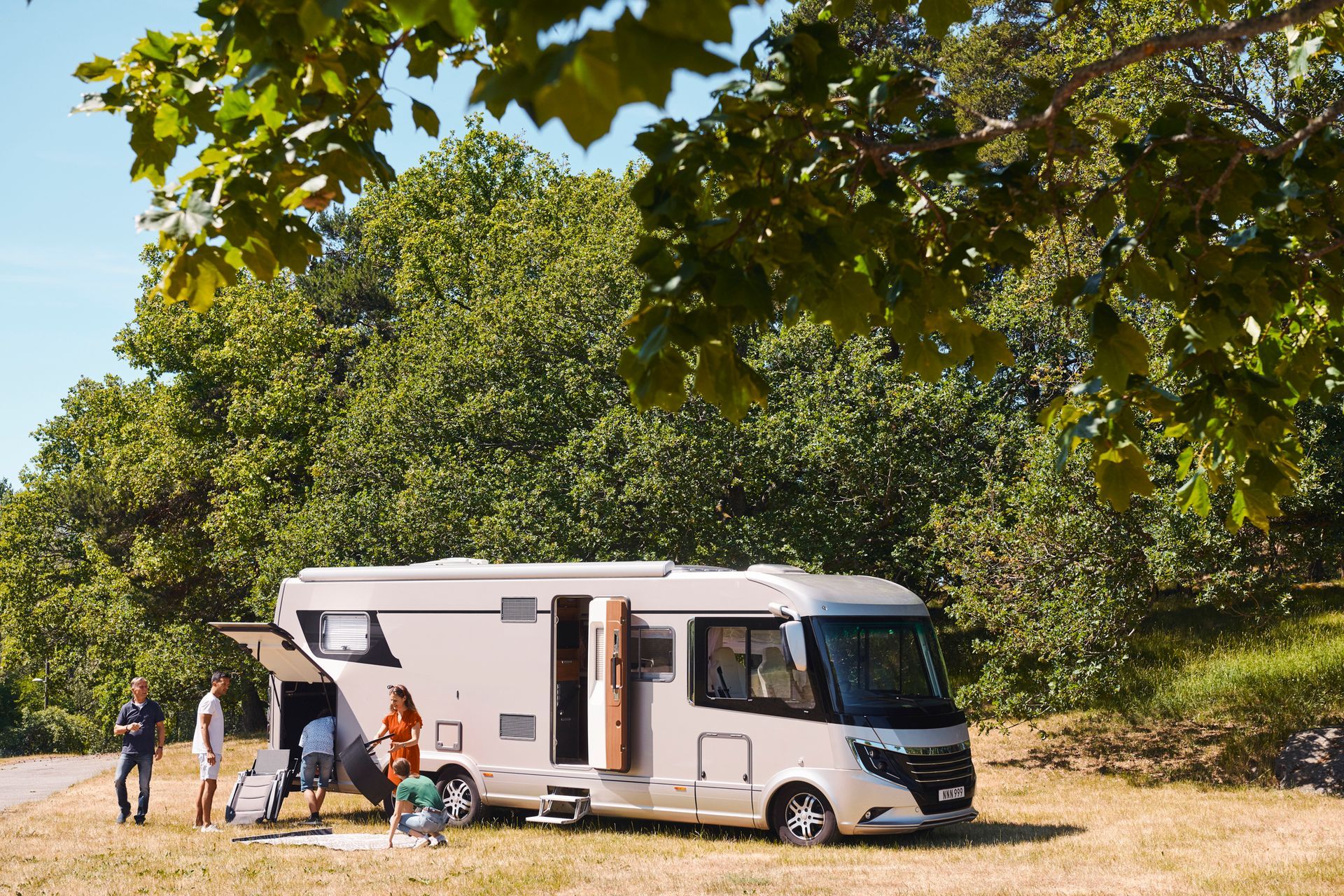 A family camping beside a white RV in a grassy area, surrounded by green trees.