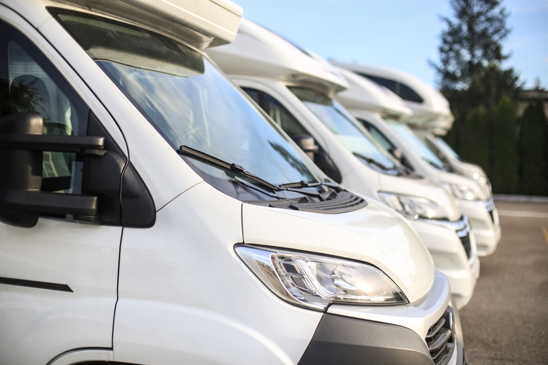 White RVs parked in a row, angled view of front ends, sunny outdoors.