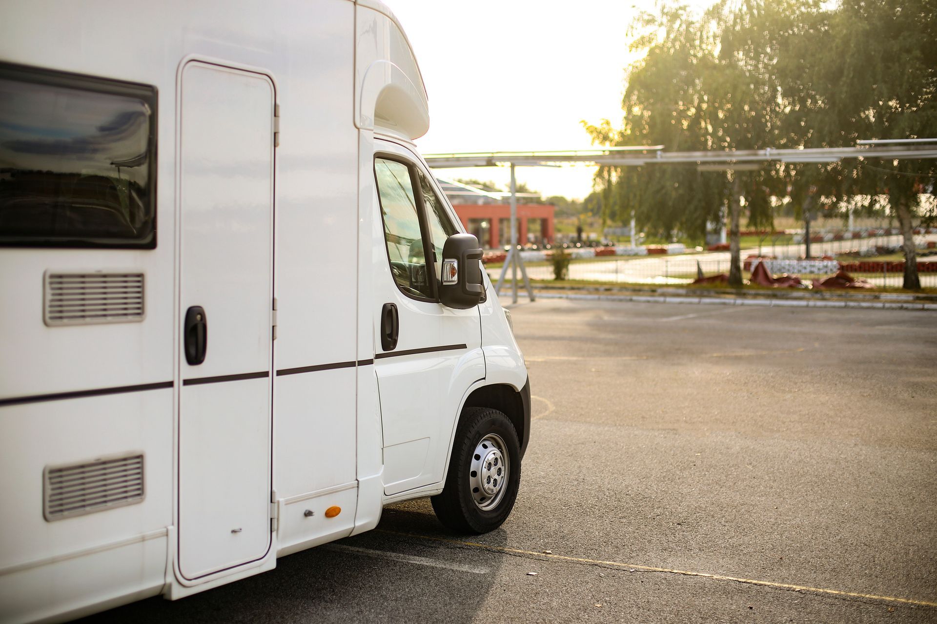 White RV parked in a paved lot with a blurred background of a building and trees.