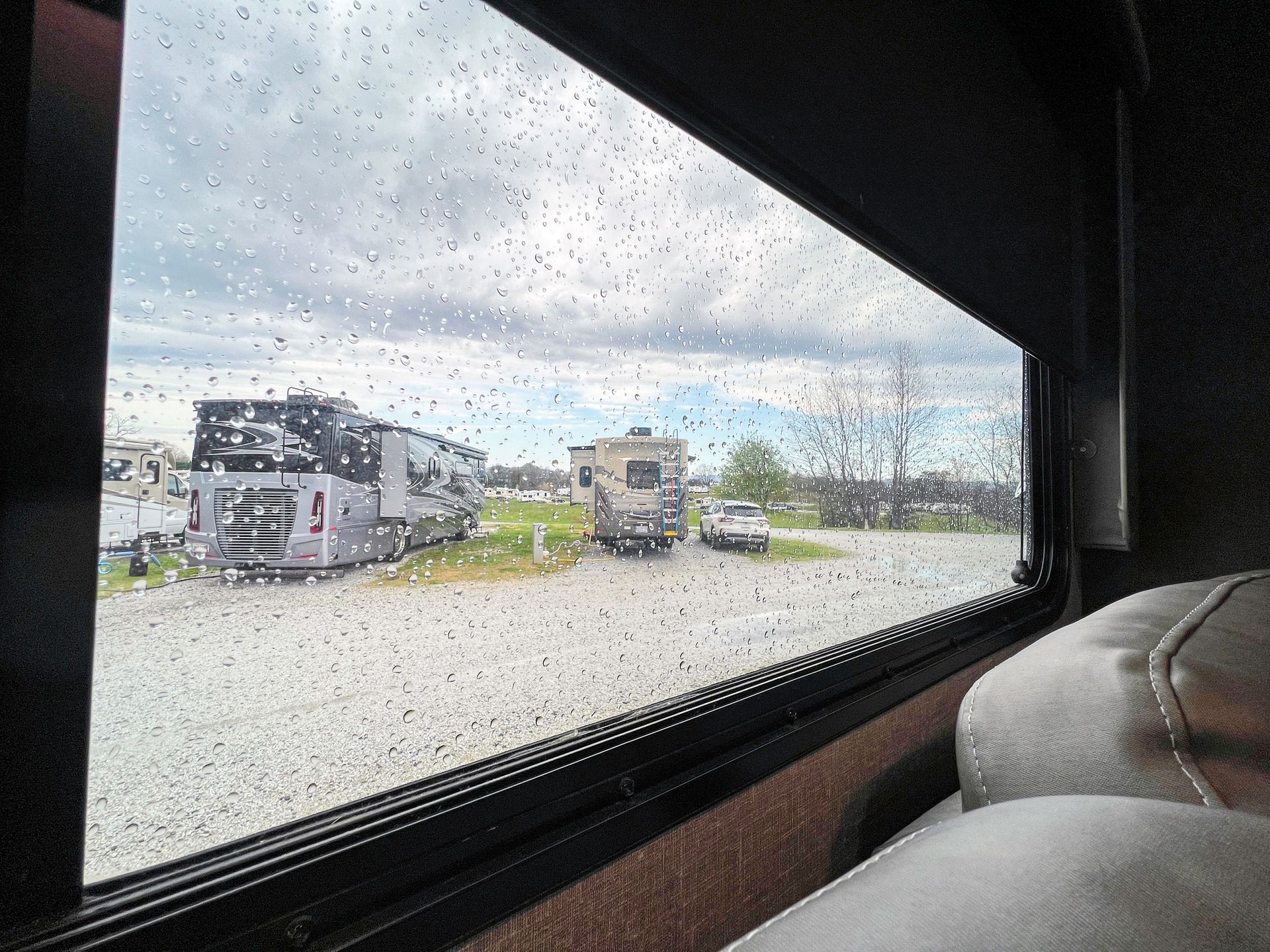 Rainy view through RV window, showing parked RVs and a car on a gray, overcast day.