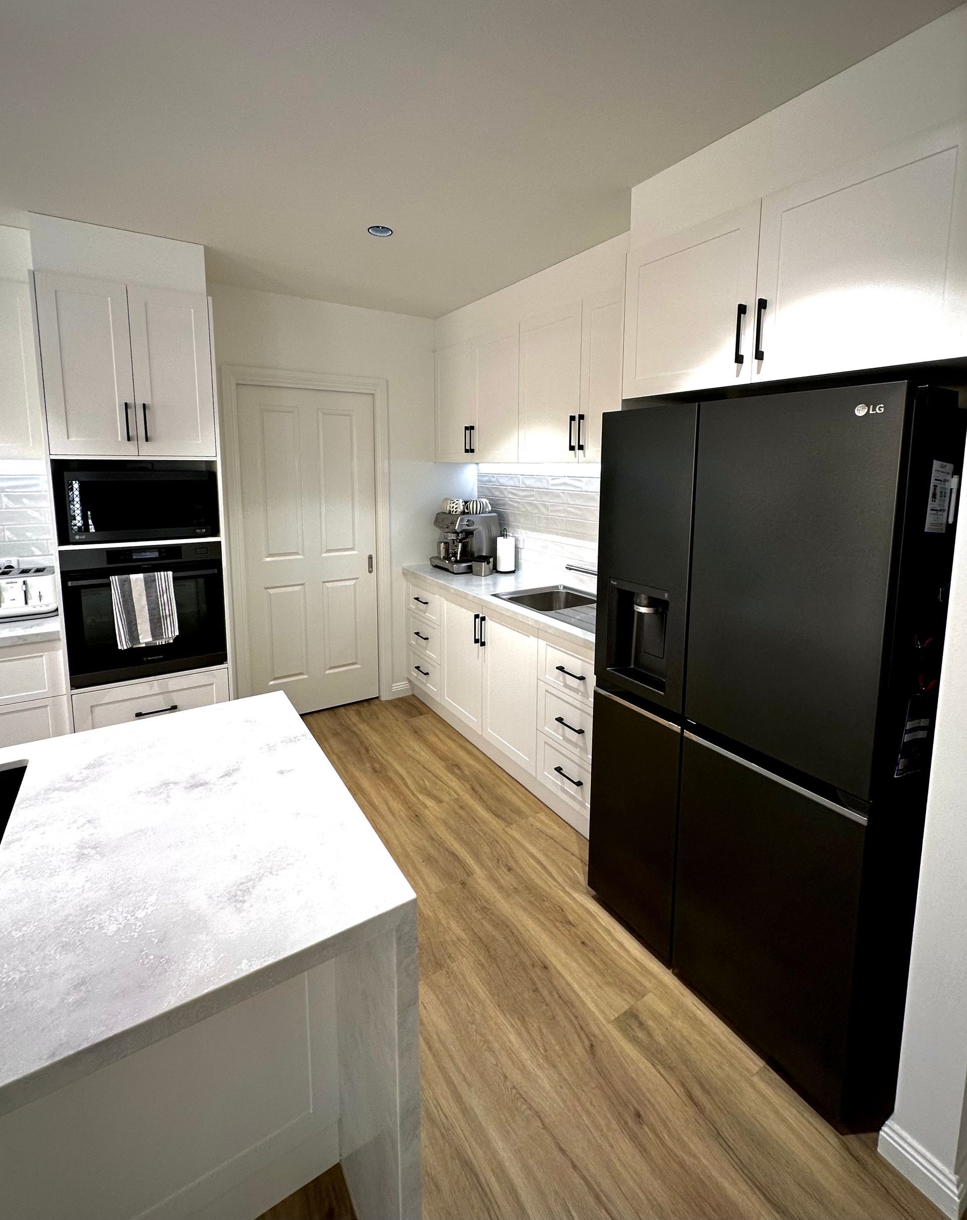 A kitchen with white cabinets and a black refrigerator.