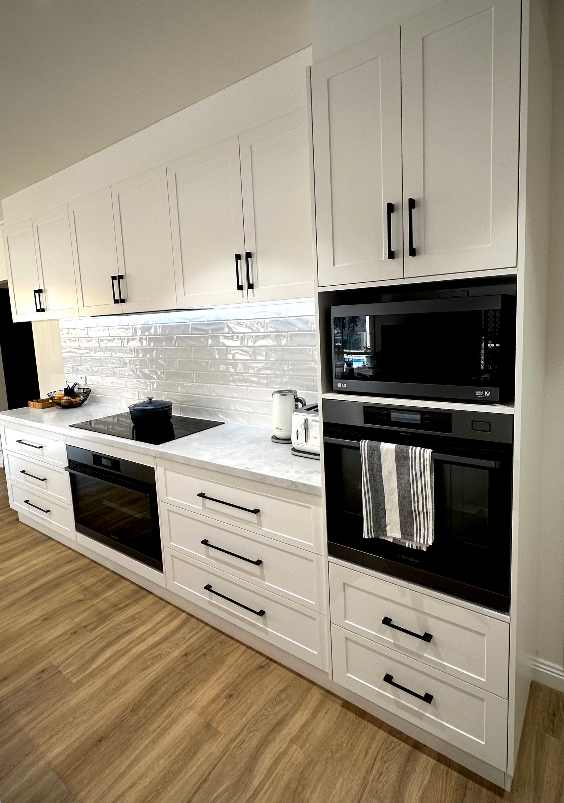A kitchen with white cabinets , black appliances , and wooden floors.