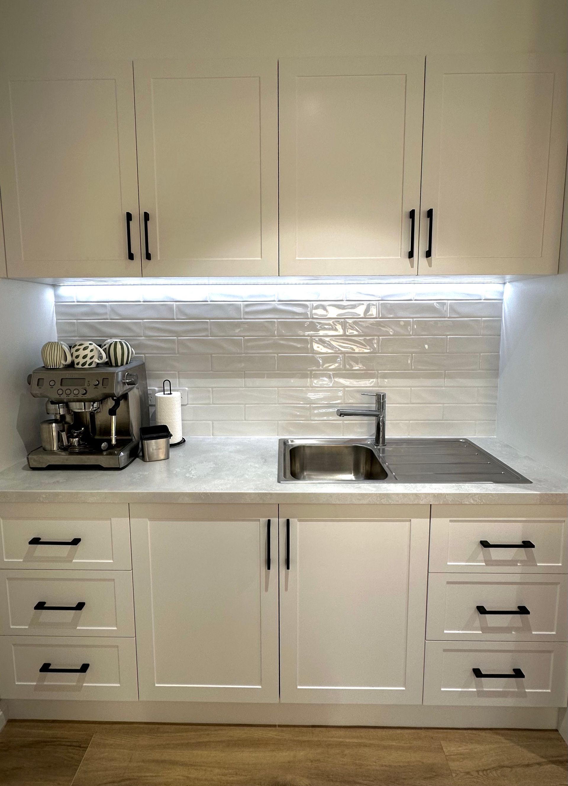 A kitchen with white cabinets , a sink , and a coffee maker.