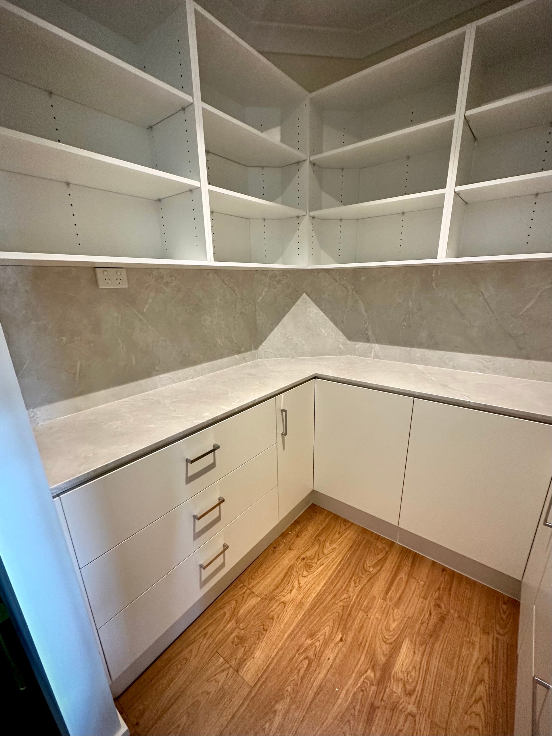 An empty walk in closet with white shelves and wooden floors.