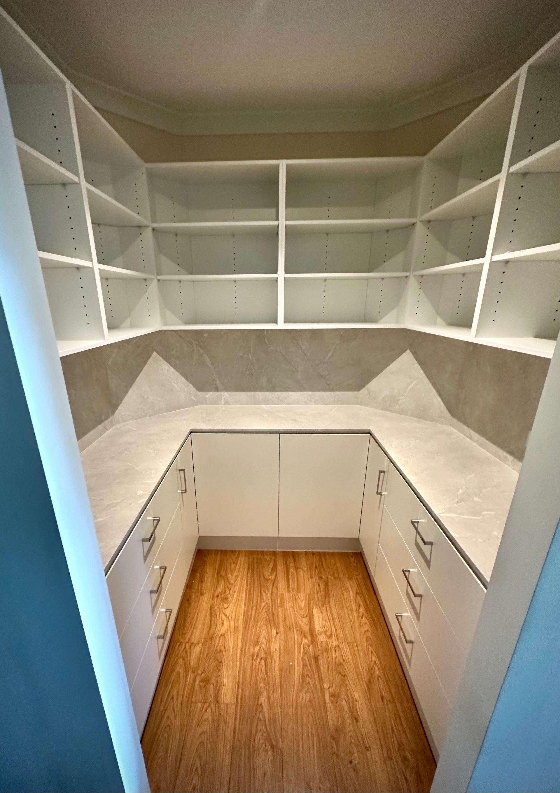 A pantry with lots of shelves and drawers and a wooden floor.