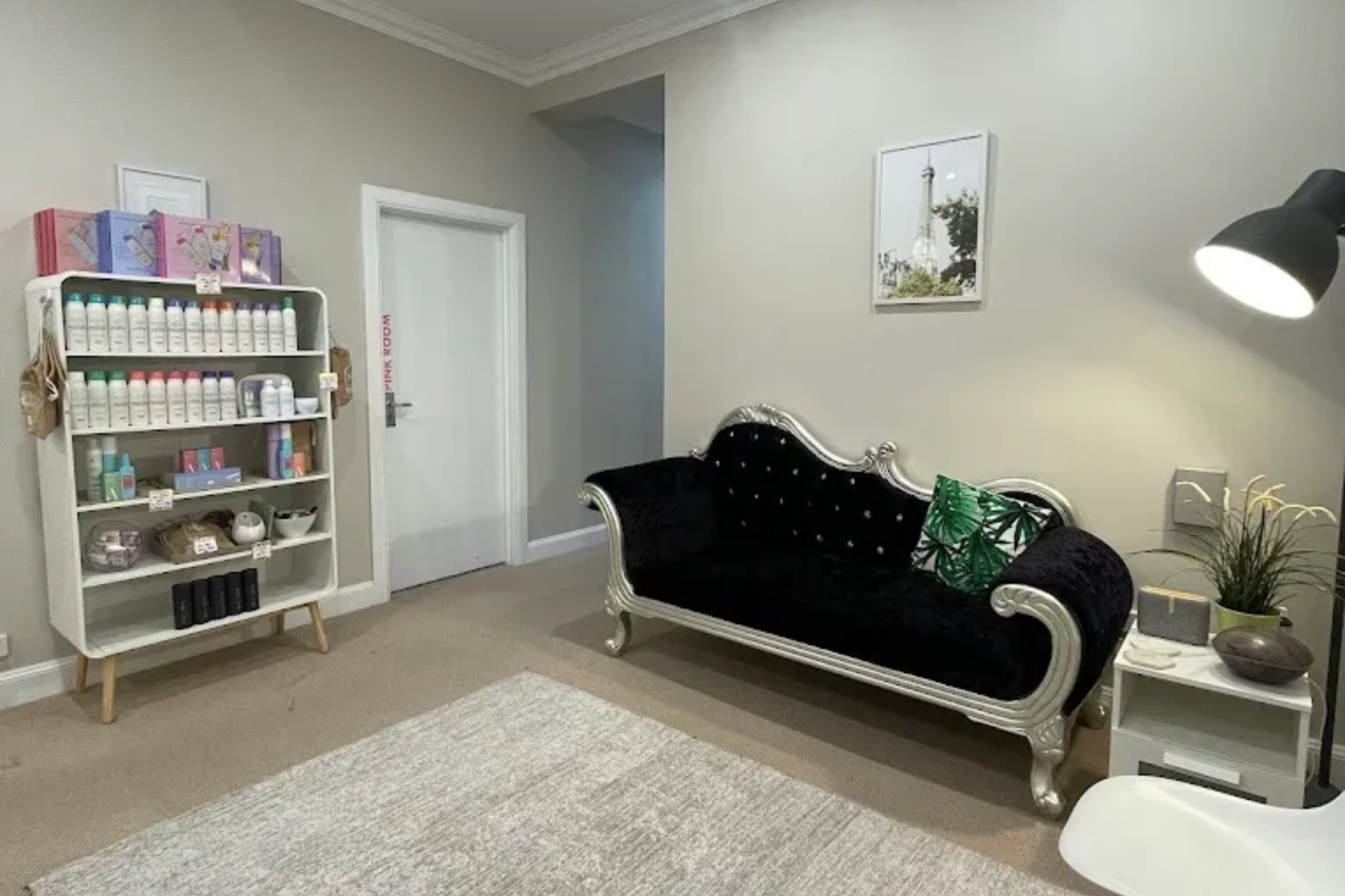 Salon interior with product shelves, black chaise lounge, and white door.