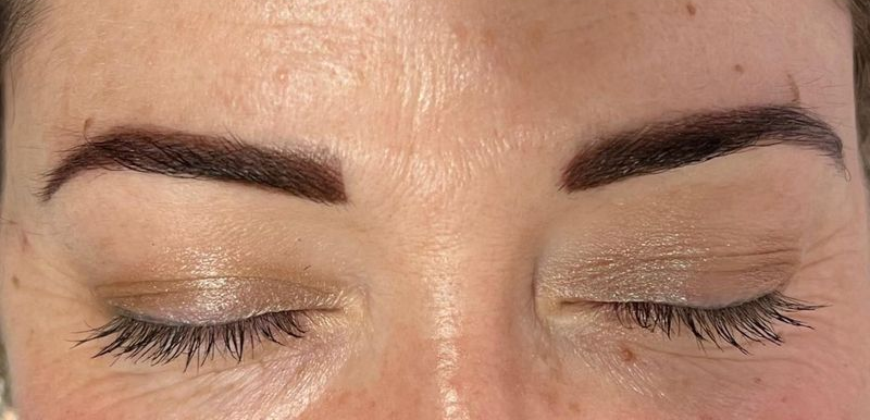 Closed eyes with dark brown, filled-in eyebrows. Skin has fine lines and is pale.