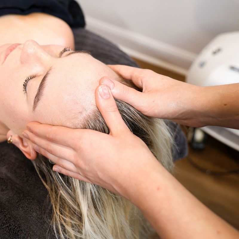 Person receiving head massage, eyes closed, hands on forehead.