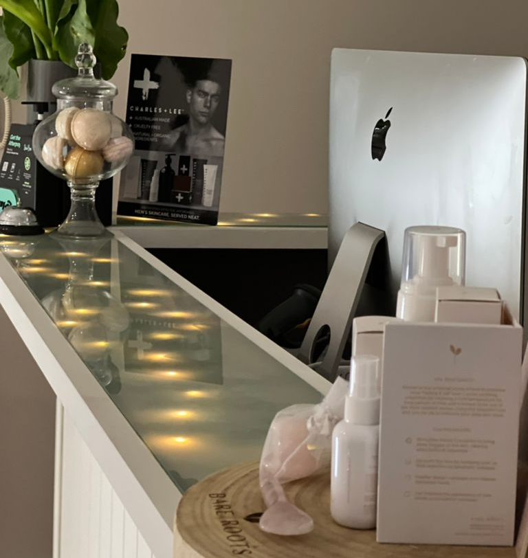 A counter with skincare products, a computer, and a decorative jar. Lit from below, items appear on a white surface.