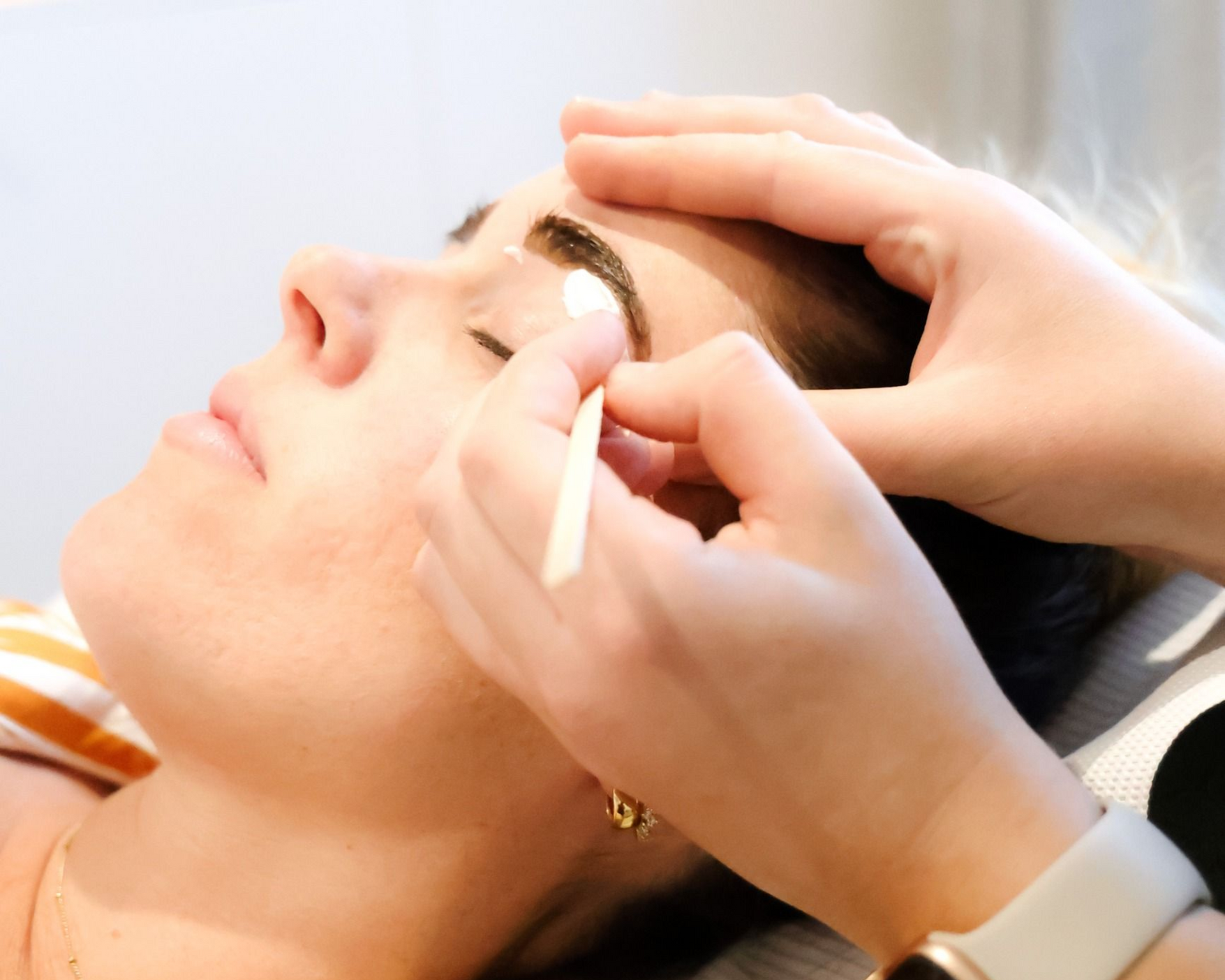 A person having their eyebrow worked on with a cotton swab; a light-skinned person in a salon setting.
