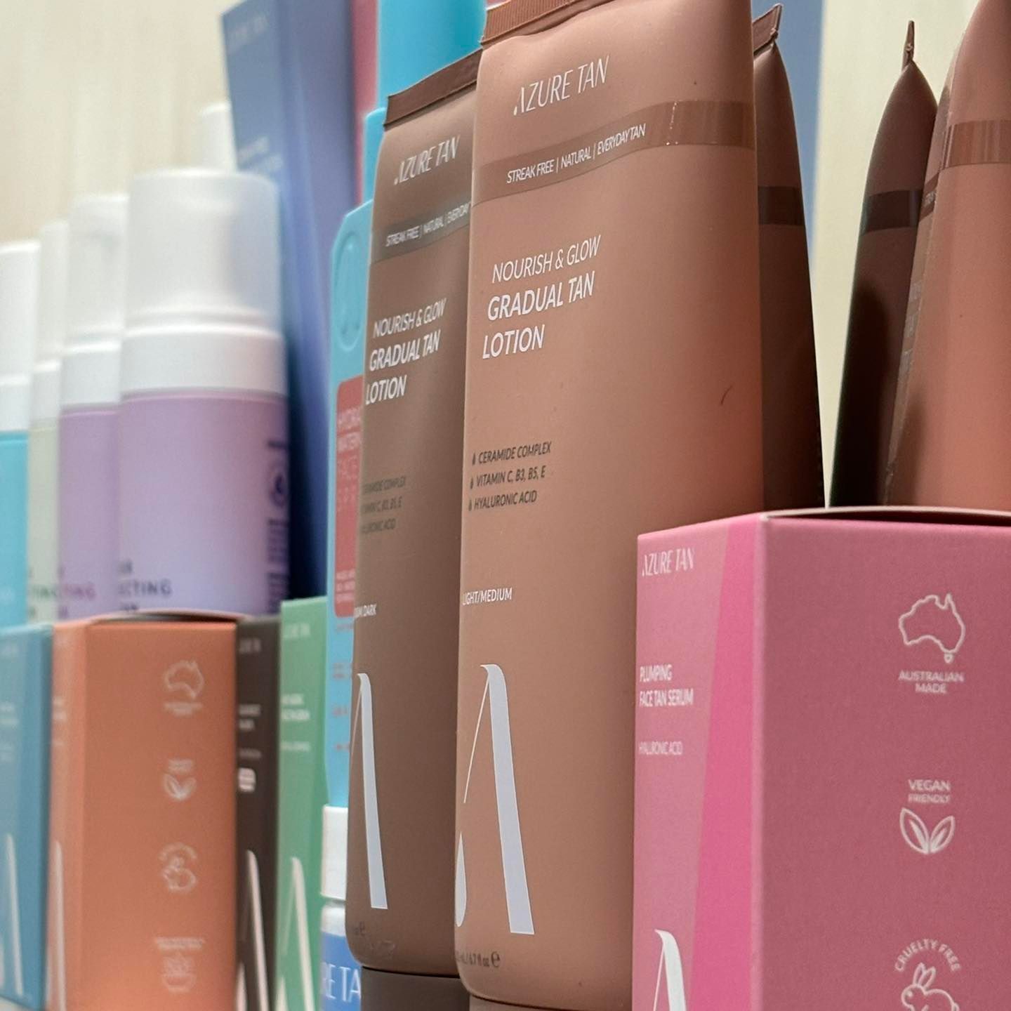 Tanned-colored lotion tubes and pink boxes for skincare products, with other cosmetic items in the background.