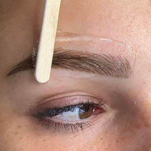Eyebrow waxing: a wooden stick applies clear wax to a person's eyebrow.