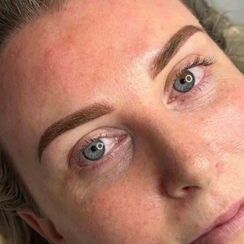 Close-up of a person's face; has newly-done, brown, shaped eyebrows, blue eyes, and visible skin texture.