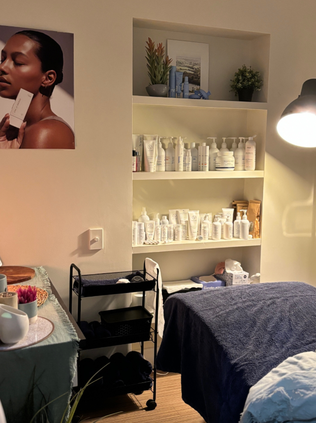 Spa room with products on shelves, a massage bed, and skincare advertising on the wall.