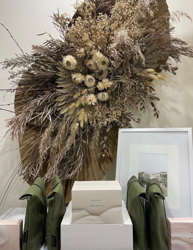 Dried floral arrangement above white framed art and a display of green items.
