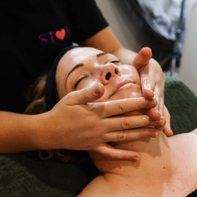 Woman receiving facial massage; hands on face, eyes closed.