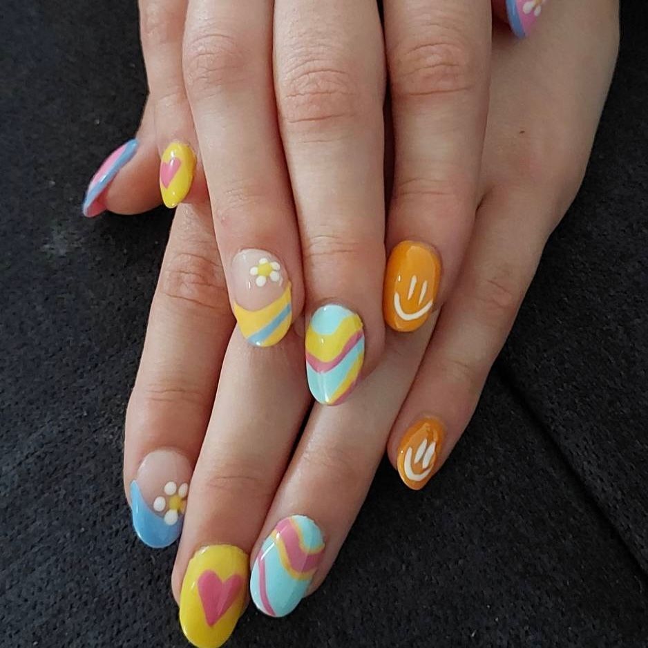 Hand with almond-shaped nails painted with colorful smiley faces, hearts, flowers, and wavy designs.