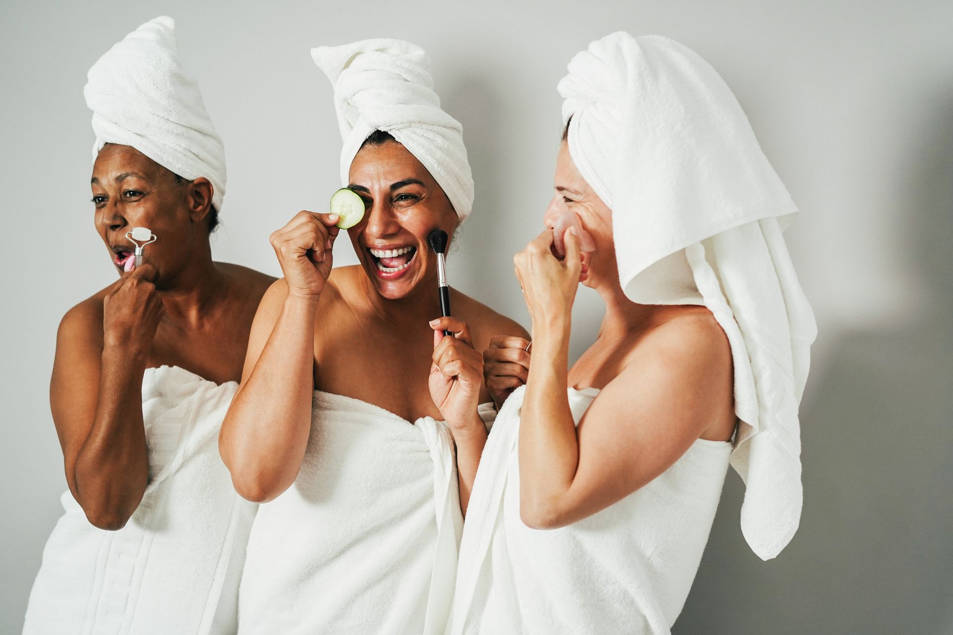 Three people wrapped in white towels, smiling and laughing during a spa day.