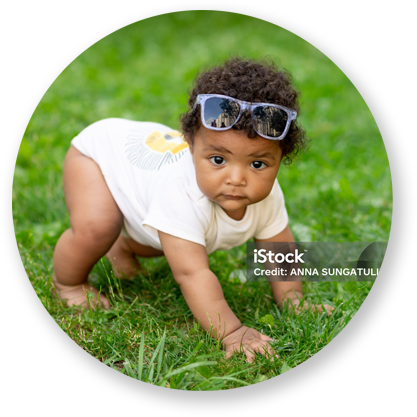 Baby wearing sunglasses crawls on green grass.