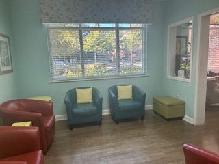 A waiting room with teal walls, red and teal armchairs, a window with blinds, and an ottoman.