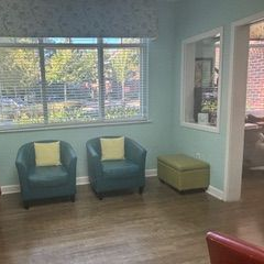 A waiting room with two teal armchairs, a green ottoman, and a large window with a view.