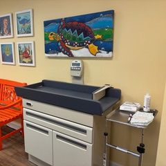 Pediatrician's office with changing station below a colorful turtle painting. Orange bench to the left.