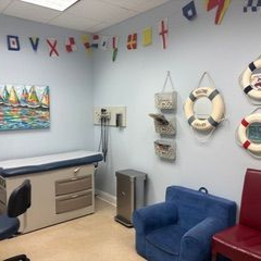 Pediatrician's office with nautical theme: exam table, armchairs, life preservers, and flags strung along the wall.