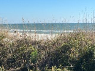 View of a beach with grass in foreground and sand, water and sky in background.