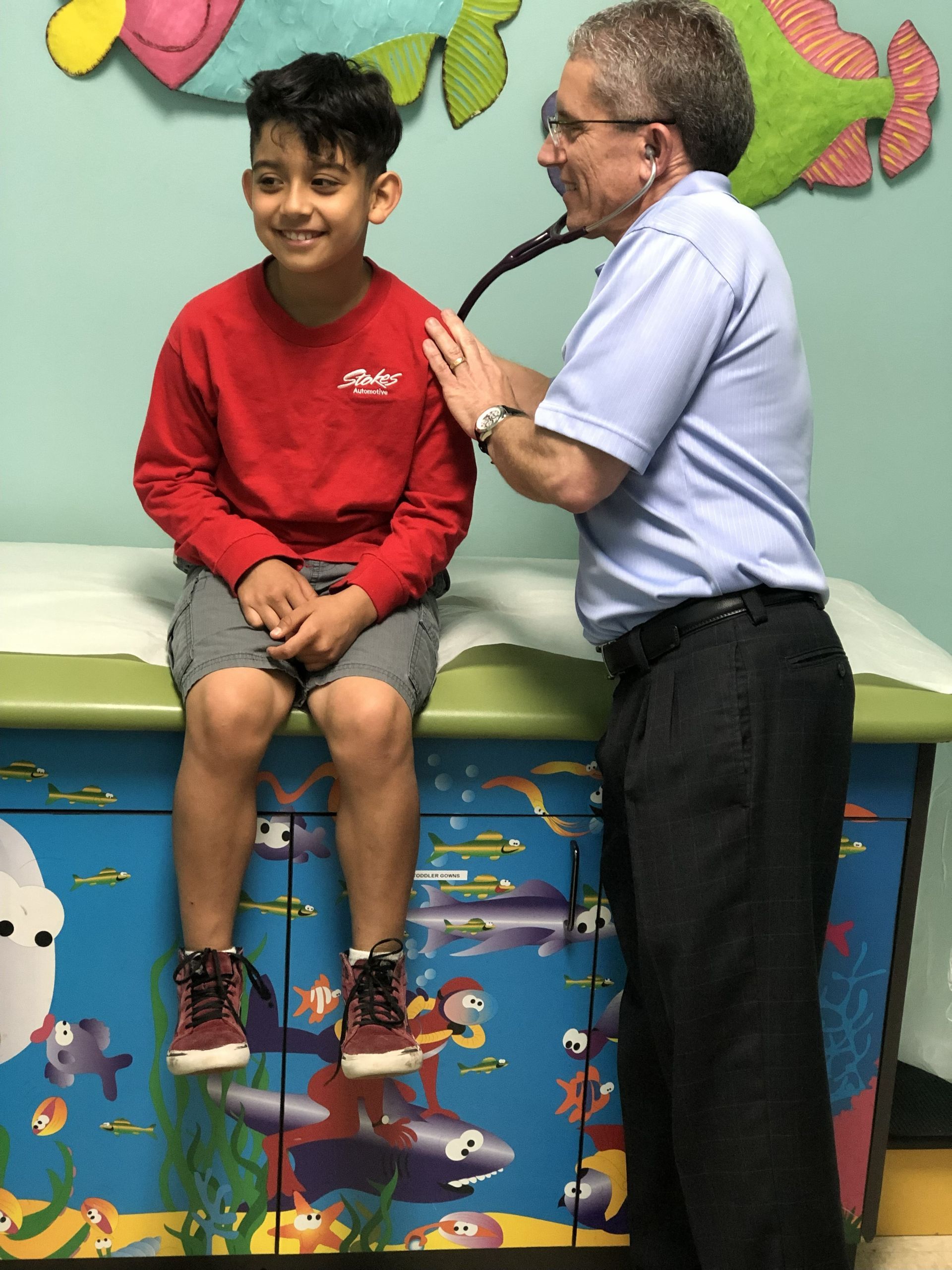 Doctor using a stethoscope on a boy sitting on a colorful examination table in a clinic.