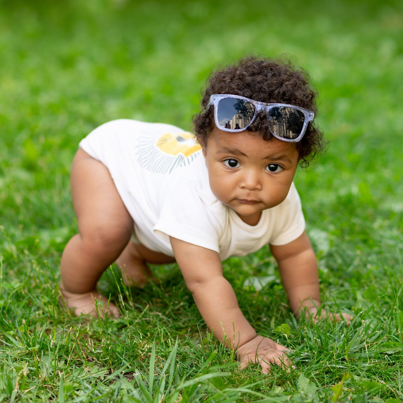 Baby wearing sunglasses crawling on green grass.
