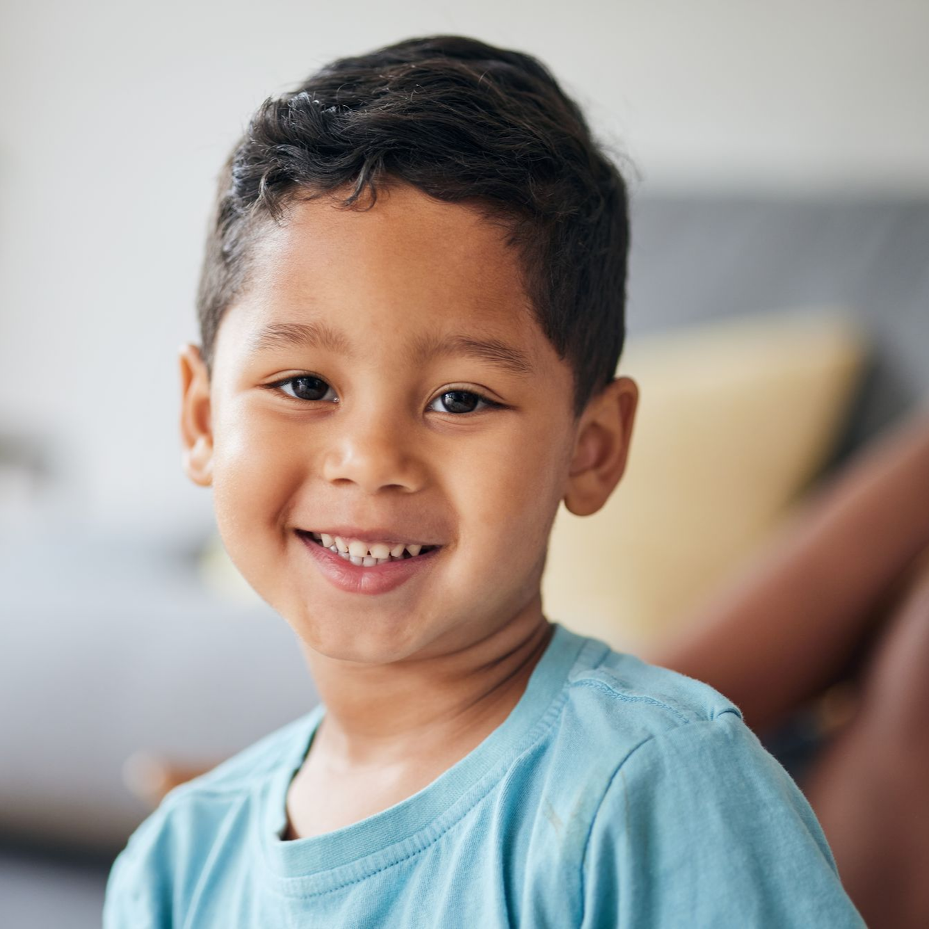 Smiling child with short dark hair in a blue shirt indoors.