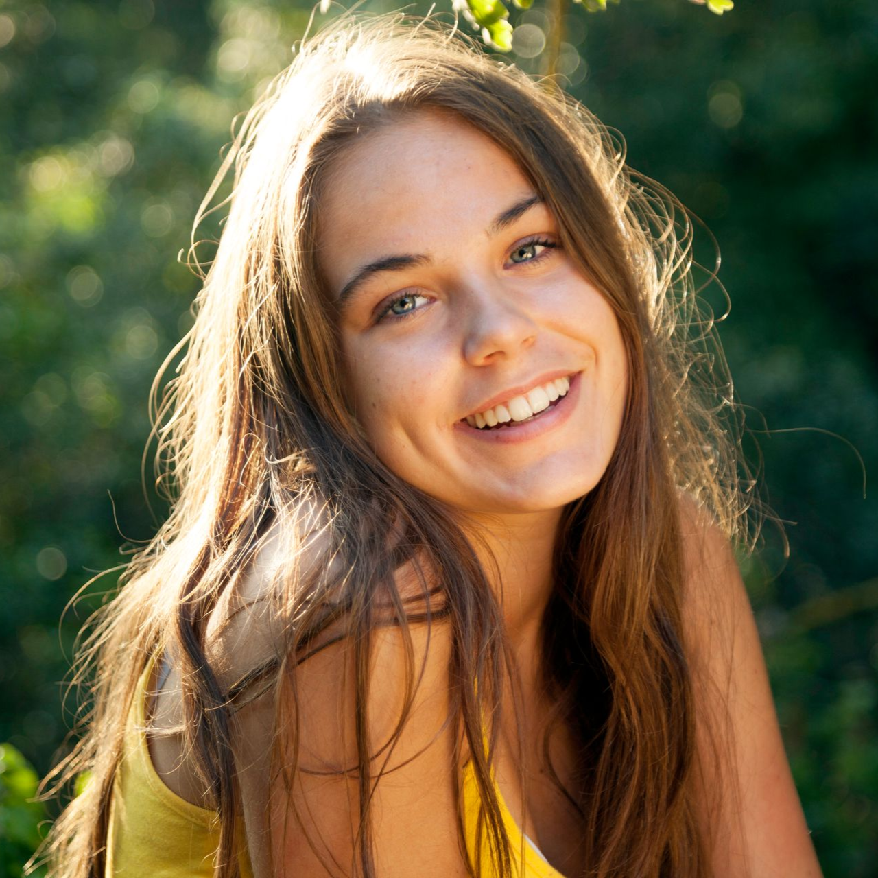 Woman with long brown hair smiles broadly outdoors.