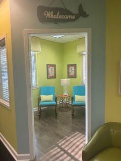 A doorway leading to a waiting area with two blue chairs, artwork, and a whale sign.