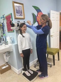 A healthcare provider measures a child's height with a stadiometer in an examination room.