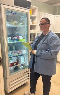 Woman in blue scrubs stands by a ClinCool refrigerator in a medical setting, holding a clipboard.
