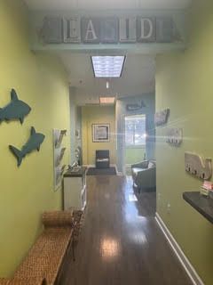 Hallway with green walls, shark decorations, and a bench leading to a waiting area with chairs and a window.